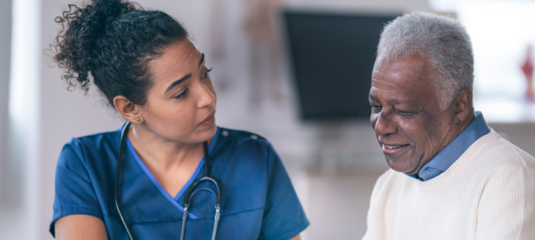 How Empowerly helps participants (Image shows a woman wearing nursing scrubs and a stethoscope speaking to an elderly male patient with dark skin.)