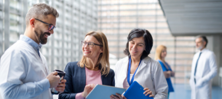 How Empowerly helps sites (Image shows a group of doctors wearing lab coats, holding various folders and conversing.)